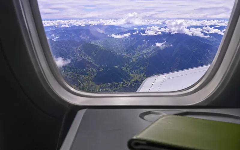 Airplane wing over mountains with a green passport holder on the tray table